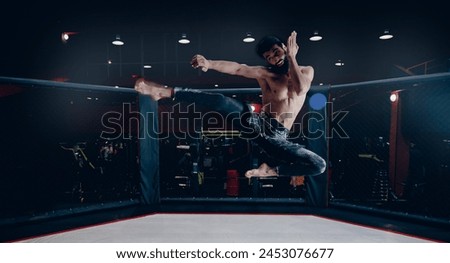MMA Training of fighter without rules in octagon cage, man makes kick in flight on dark background.
