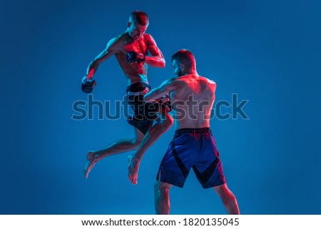 MMA. Two professional fighters punching or boxing isolated on blue studio background in neon. Fit muscular caucasian athletes or boxers fighting. Sport, competition and human emotions, ad.