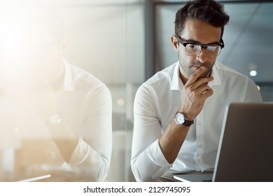 Mmm...I wonder. Cropped shot of a handsome young businessman looking thoughtful while working on his laptop in the office. - Shutterstock ID 2129745095