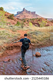 MOAB, UTAH - FEBRUARY 5, 2022: Young Man Crossing A Stream In The Desert Under Rock Feature