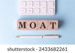 MOAT on a wooden cubes with pen and calculator, financial concept
