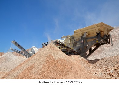 Mobil Crusher.  Conveyor Belt Of A Working Mobile Crusher Machine, Close-up, With Blown Away By The Wind White Stone Dust Against A Blue Sky.