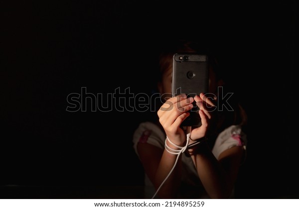 Mobile addiction and digital dependence
concept. Young girl tied with cell phone charger cord and holds
smartphone. Copy space for design. Horizontal
image.