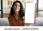 Mobile Advertisement. Happy Beautiful Woman Showing Big Blank Smartphone At Camera While Sitting On Couch At Home, Young Female Demonstrating Phone With White Screen For App Design, Collage, Mockup