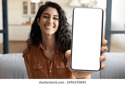 Mobile Advertisement. Happy Beautiful Woman Showing Big Blank Smartphone At Camera While Sitting On Couch At Home, Young Female Demonstrating Phone With White Screen For App Design, Collage, Mockup