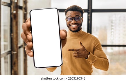 Mobile app advertisement. Black man showing and pointing at big white empty smartphone screen, standing in office, mockup, closeup. Check this out, cellphone display template