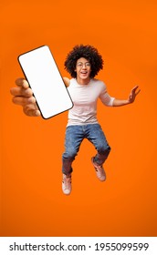 Mobile App Advertisement. Excited Teen Black Guy Showing Smartphone With Empty Screen, Jumping In Air On Orange Studio Background, Copy Space. Check This Out, Cellphone Display Mockup