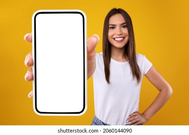 Mobile App Advertisement. Excited Woman Showing White Empty Smartphone Screen Recommending App Posing Over Orange Studio Background, Smiling To Camera. Check This Out, Cellphone Display Mock Up