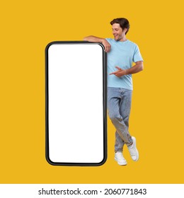 Werbung für mobile App. Voller Körper Länge des glücklichen Mannes, der auf dem riesigen weißen, leeren Smartphone-Bildschirm auf orangefarbenem Studio-Hintergrund leuchtet. Jetzt ausprobieren, Handy-Display-Movie-Up