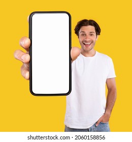 Mobile App Advertisement. Handsome Excited Man Showing White Empty Smartphone Screen Recommending App Posing Over Orange Studio Background, Smiling To Camera. Check This Out, Cellphone Display Mock Up