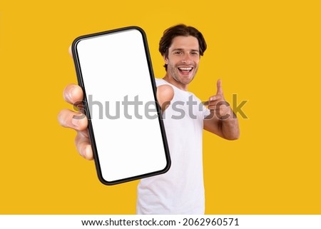 Mobile App Advertisement. Handsome Excited Man Showing Pointing At White Empty Smartphone Screen Posing Over Orange Studio Background, Smiling To Camera. Check This Out, Cellphone Display Mock Up Foto stock © 
