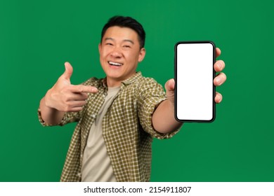 Mobile app advertisement. Happy asian mature man pointing at empty smartphone screen, showing space for your design, posing over green background, mockup. Check this out - Powered by Shutterstock