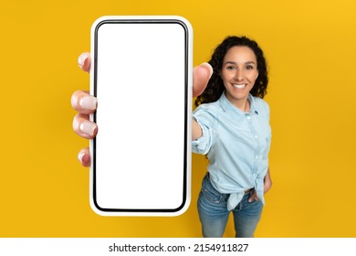 Mobile App Advertisement. Happy Woman Showing Big White Empty Smartphone Screen Close Up To Camera, Recommending App On Orange Studio Wall, Selective Focus On Hand. Check This Out, Cellphone Display