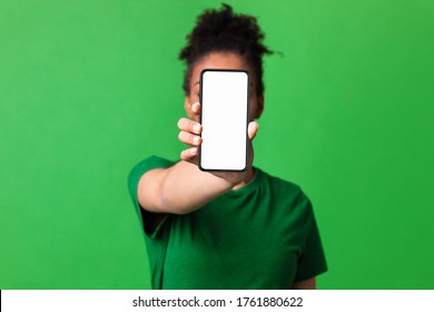 Mobile App Advertising. African woman showing blank cellphone screen, mockup, selective focus, green studio wall - Powered by Shutterstock