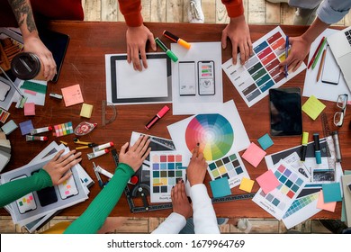 Mobile app design. Top view of designers discussing sketches, choosing colors from palettes lying on the desk while having a meeting in the modern office. Creative agency concept