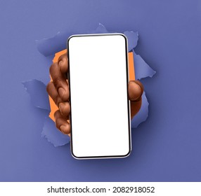 Mobile App, Great Offer. Closeup Of Black Male Hand Holding Smartphone With White Empty Screen Showing Device Close To Camera Breaking Through Paper Sheet. Gadget Display With Free Copy Space, Mock Up