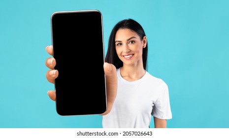 Mobile App Mockup. Beautiful Young Woman Showing Big Smartphone With Black Blank Screen, Smiling Female Demonstrating Free Copy Space For Your Design Or Advertisement, Posing Over Blue Background