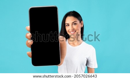 Mobile App Mockup. Beautiful Young Woman Showing Big Smartphone With Black Blank Screen, Smiling Female Demonstrating Free Copy Space For Your Design Or Advertisement, Posing Over Blue Background