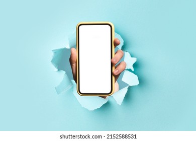 Mobile App Promo, Great Offer. Closeup Of Hand Holding Cell Phone With White Empty Screen Showing Device To Camera Breaking Through Blue Paper Sheet. Blank Display With Free Copy Space, Mock Up Banner