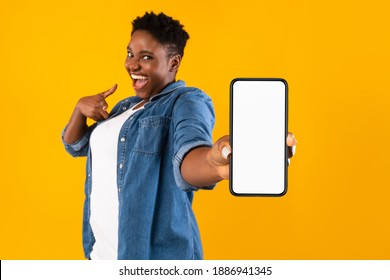 Mobile Application Ad. Excited African Woman Showing Phone Empty Screen Recommending App Standing Over Yellow Studio Background, Smiling To Camera. Cellphone Display Mockup, Check This Apps - Powered by Shutterstock