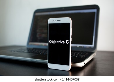 Mobile application development, Objective C programming language for mobile development. Workplace of programmer, tester, laptop, and smartphone