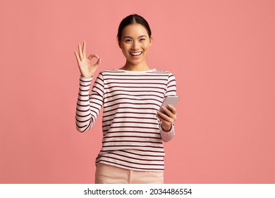 Mobile Banking. Happy Young Asian Woman Holding Smartphone And Showing Ok Gesture, Cheerful Korean Female Enjoying Making Payments Online While Standing Isolated Over Pink Background, Copy Space