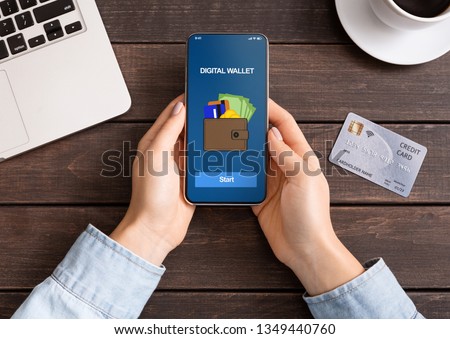 Mobile banking. Woman holding smartphone with digital wallet application. credit card on table, top view