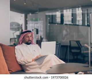 Mobile business communication and entrepreneurship. Arab businessman talking on smartphone and using laptop computer at workplace at home office