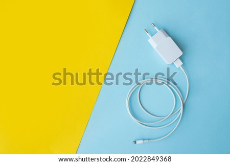 Mobile charger and USB Cable on blue and yellow background. Top view.