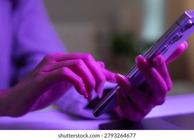 Mobile communication and digital technology concept. Close-up of person using smartphone with colorful neon lighting indoors. smartphone, messaging, connectivity, mobile, technology