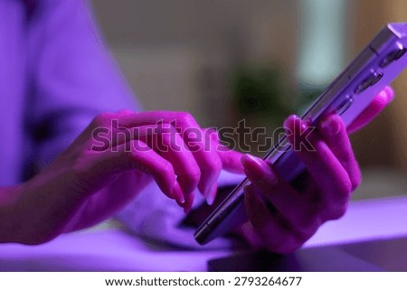 Mobile communication and digital technology concept. Close-up of person using smartphone with colorful neon lighting indoors. smartphone, messaging, connectivity, mobile, technology