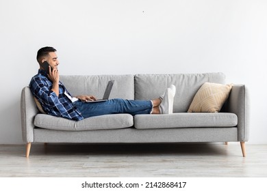 Mobile Communication. Smiling Arabic Male Freelancer Talking On Cellphone Working On Pc At Home Office, Positive Guy Using Computer Having Phone Conversation, Enjoying Distance Job, Sitting On Sofa - Shutterstock ID 2142868417