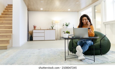 Mobile Communication. Smiling Black Female Freelancer Talking On Cellphone Working On Pc At Home Office, Positive Lady Using Computer Having Phone Conversation, Enjoying Distance Job, Banner Panorama