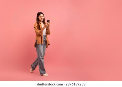 Mobile Communication. Smiling Teen Girl Walking With Smartphone Over Pink Background, Happy Female Teenager Browsing Internet Or Messaging With Friends, Full Length Shot, Copy Space - Powered by Shutterstock