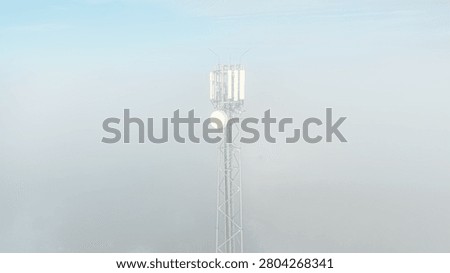 Mobile communication tower emerging from dense morning fog