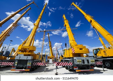 Mobile construction cranes with yellow telescopic arms and big tower cranes in sunny day with white clouds and deep blue sky on background, heavy industry 