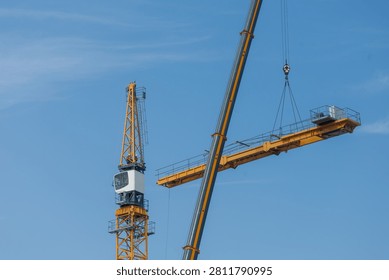 Mobile crane lifting tower crane section at construction site under blue sky