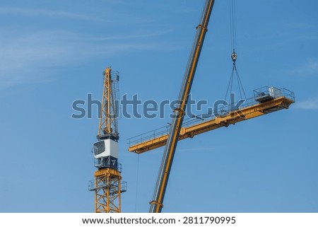 Mobile crane lifting tower crane section at construction site under blue sky