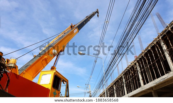 Mobile cranes\
at construction sites. A large yellow truck mounted crane sits\
beside a building under construction and has low voltage lines on a\
cloudy sky background. Selective\
focus
