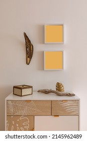 Mobile detail with drawers and various objects placed on top. Above the cabinet there are two empty frames. White wall.