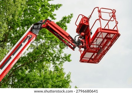 Mobile elevating work platform basket made of red steel mesh raised in the air for utility engineering and construction operations near tree canopy