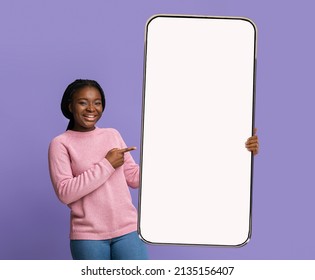 Mobile Mockup. Black lady pointing at big white smartphone screen while posing over purple background, happy african lady demontrating blank cellphone with copy space for advertisement, collage