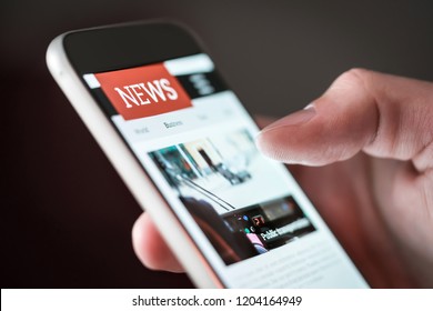 Mobile news application in smartphone. Man reading online news on website with cellphone. Person browsing latest articles on the internet. Light from phone screen. - Shutterstock ID 1204164949