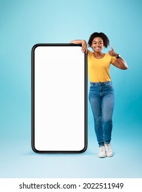 Mobile Angebot. Happy black lady, die sich auf riesiges Handy mit leerem weißem Bildschirm stützt, die Daumen hochhält, coole neue App oder Website empfiehlt, Platz für Ihre Anzeige bietet, Mock-up