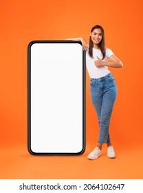 Mobile Offer. Happy woman leaning on huge cellphone with blank white screen, showing thumb up gesture, recommending great new app or website for phone, offering space for ad, mock up, full body length