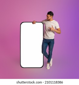 Mobile Offer. Happy Young Arab Man Leaning On Huge Cellphone With Empty White Screen, Gesturing Thumb Up, Recommending New App Or Website, Offering Blank Space For Your Ad, Mockup