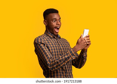 Mobile Offer. Surprised funny black guy looking at smartphone screen with excitement, emotionally reacting to online news, standing with opened mouth isolated over yellow background, copy space