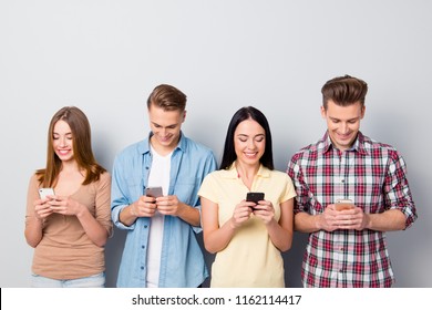 Mobile operator makes big discounts on messages! Group of four beautiful, concentrated, excited guys stand isolated on light gray background with modern cellular and writes messages check email