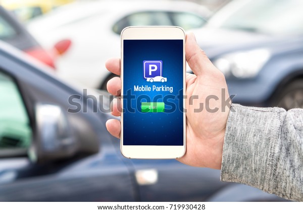Mobile parking app on smartphone\
screen facing camera. Man holding smart phone with car park\
application in hand. Internet payment online with modern\
device.