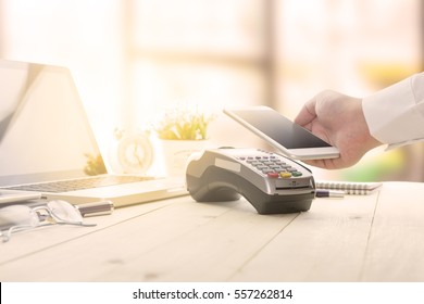 Mobile payments concept with EDC machine or credit card terminal with computer laptop and glasses. Warm toning effect.